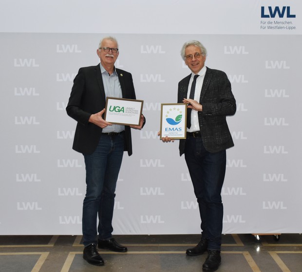 Thomas Voß (Kaufmännischer Direktor) steht mit dem LWL-Krankenhausdezernenten, Prof. Dr. Noeker vor einem grauen Hintergrund, beide halten Zertifikate