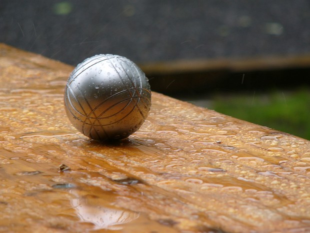 Eine silberfarbene Boulekugel liegt auf einer Holzfläche